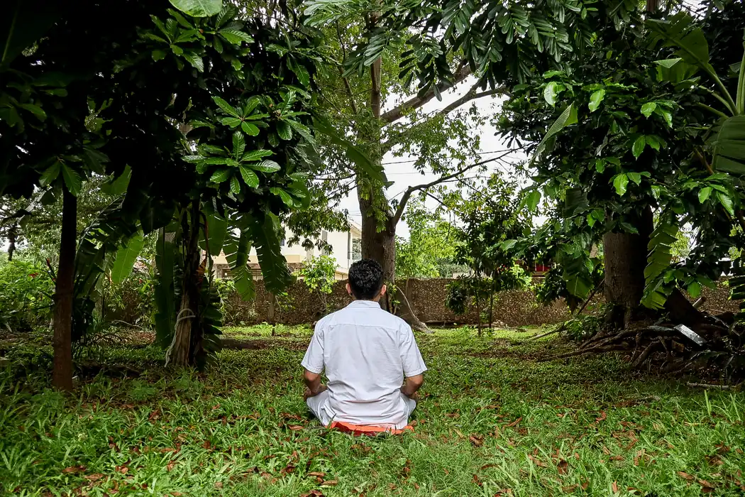 El Dr. Anuar Mena de espaldas, sentado en práctica de mindfulness entre los árboles del jardín.